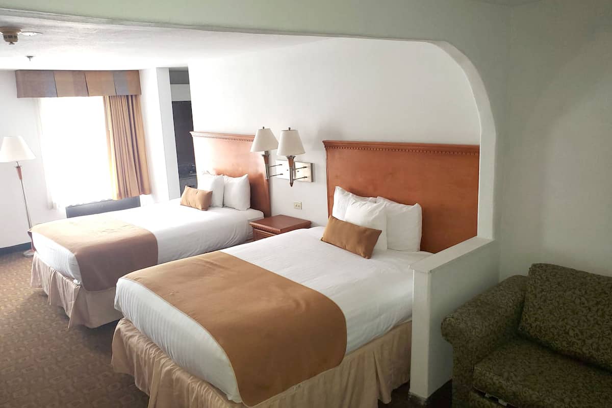 A hotel room with two beds, a sofa, and a lamp.
