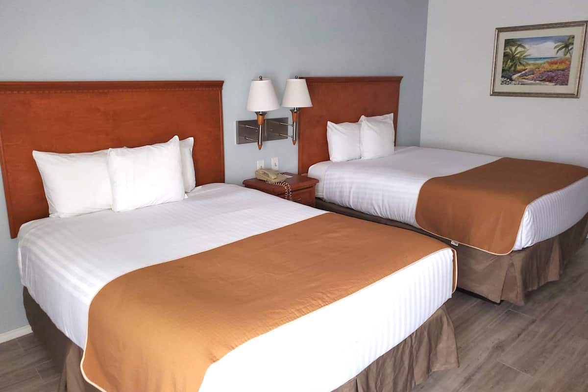 A hotel room with two beds, each with white linens and brown headboards. There is a nightstand with a lamp and a telephone between the beds.