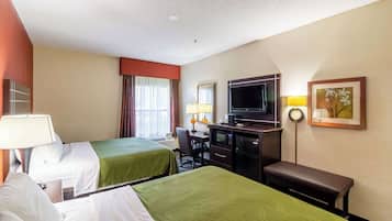 A hotel room with two beds, a desk, a television, and a bench.