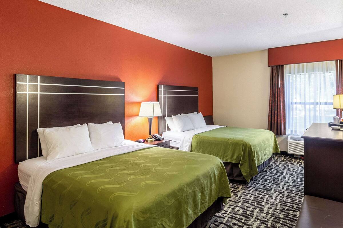 A hotel room with two beds, a desk, and a window with curtains.