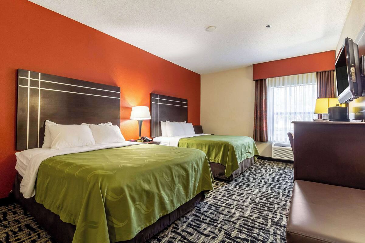 A hotel room with two beds, a TV, a desk, and a patterned carpet.