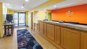 A hotel reception area with a wooden reception desk, a digital screen, and a carpeted floor.