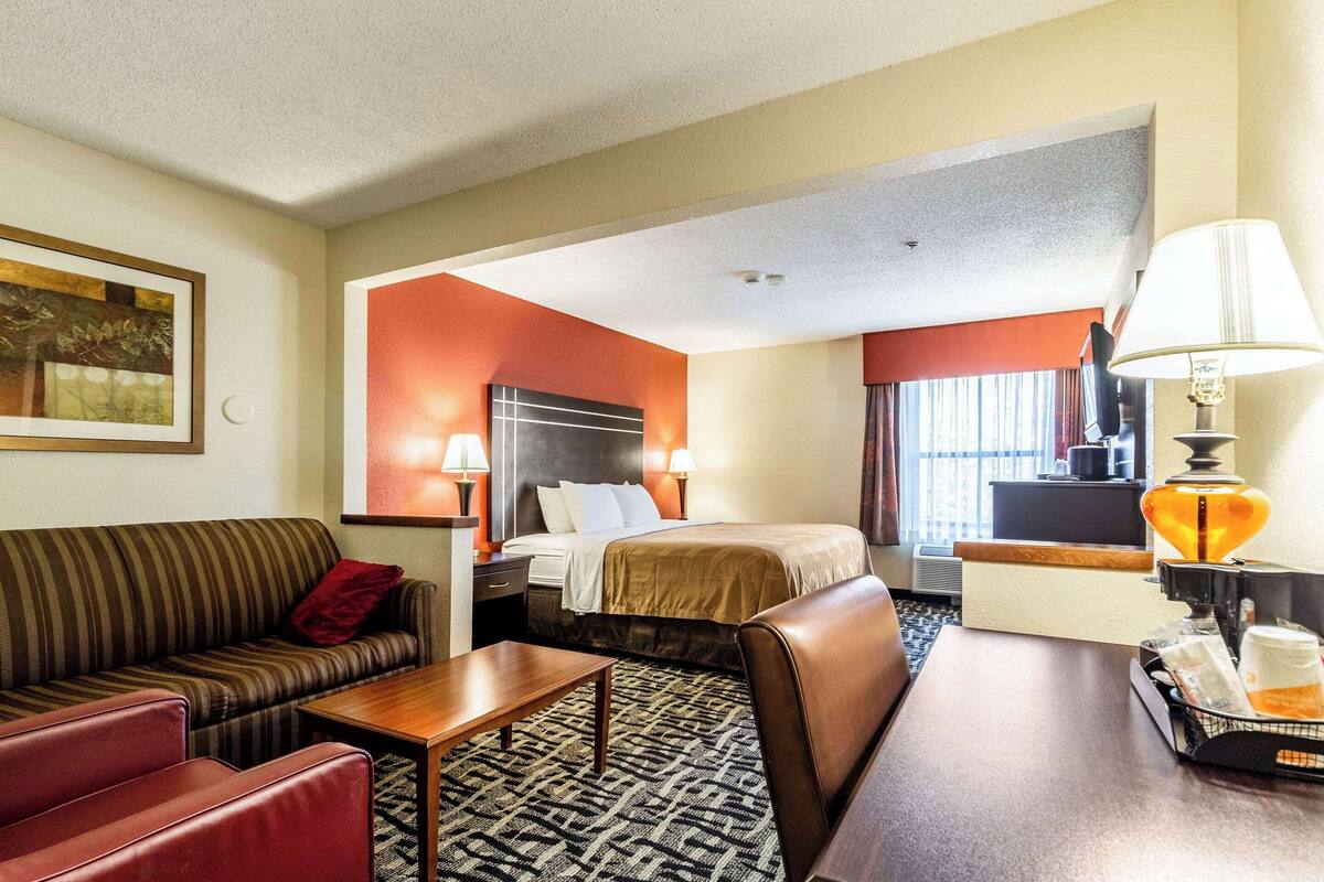 A hotel room with a bed, a sofa, a desk, and a lamp.