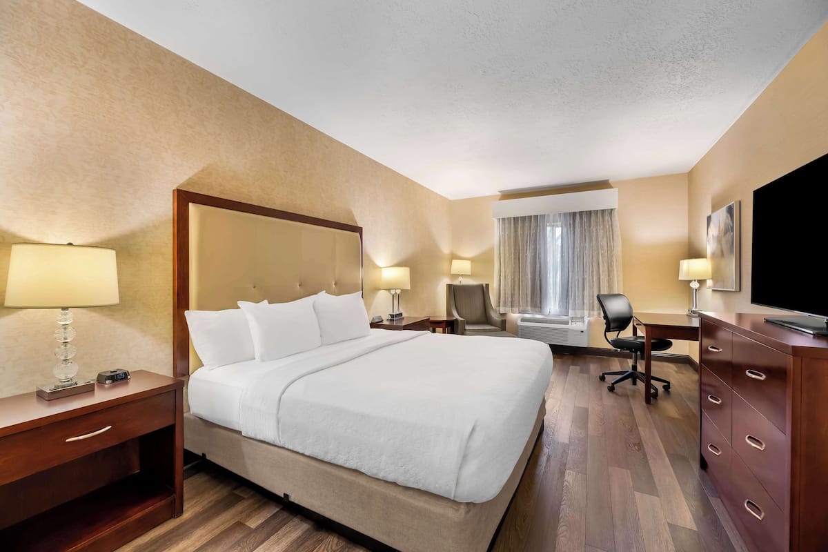 A hotel room with a large bed, bedside tables with lamps, a desk with a chair, a dresser, and a television.