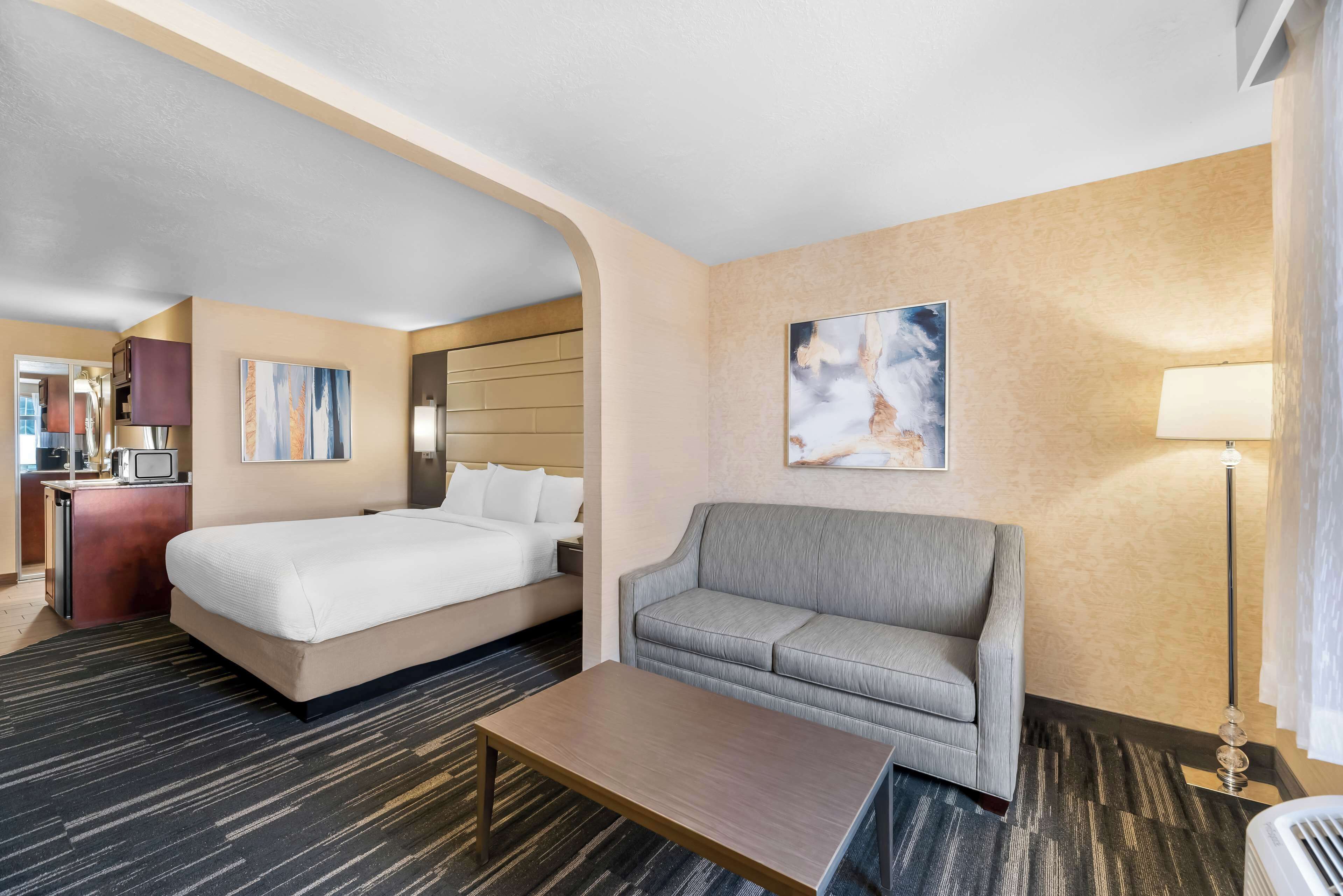 A hotel room with a bed, a sofa, a coffee table, and a desk with a lamp.
