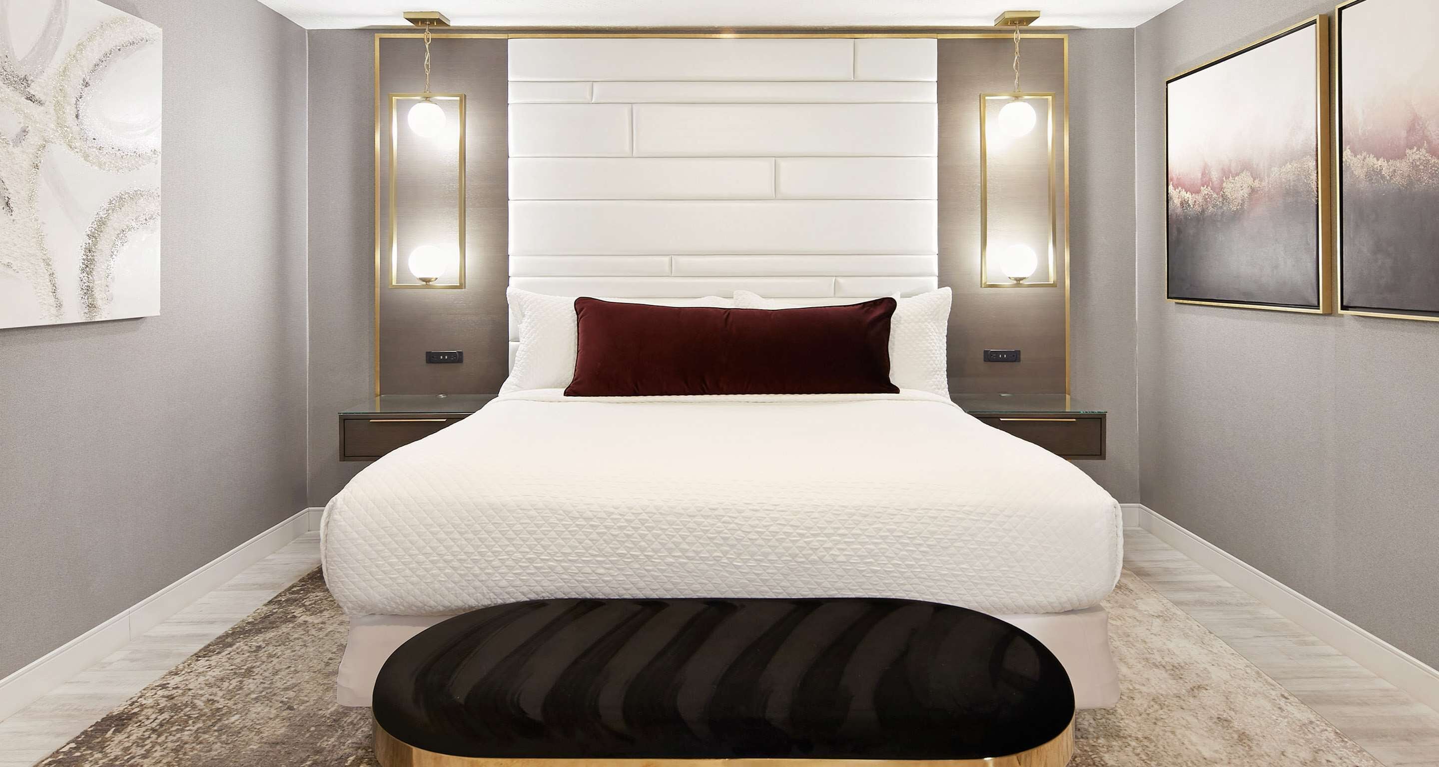 A modern bedroom with a large bed, two bedside tables, a nightstand, a decorative wall piece, and a framed picture on the wall.