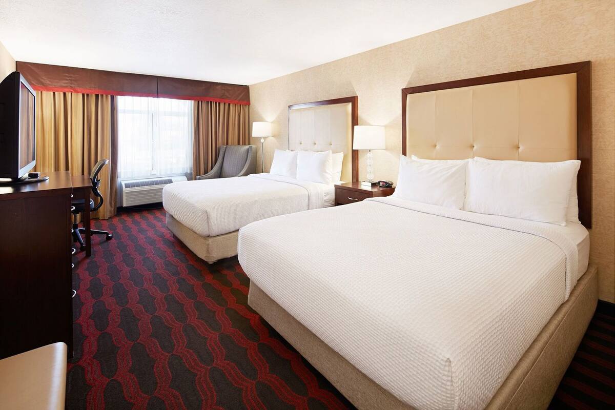 A hotel room with two beds, a desk, a chair, a TV, and a window with curtains.