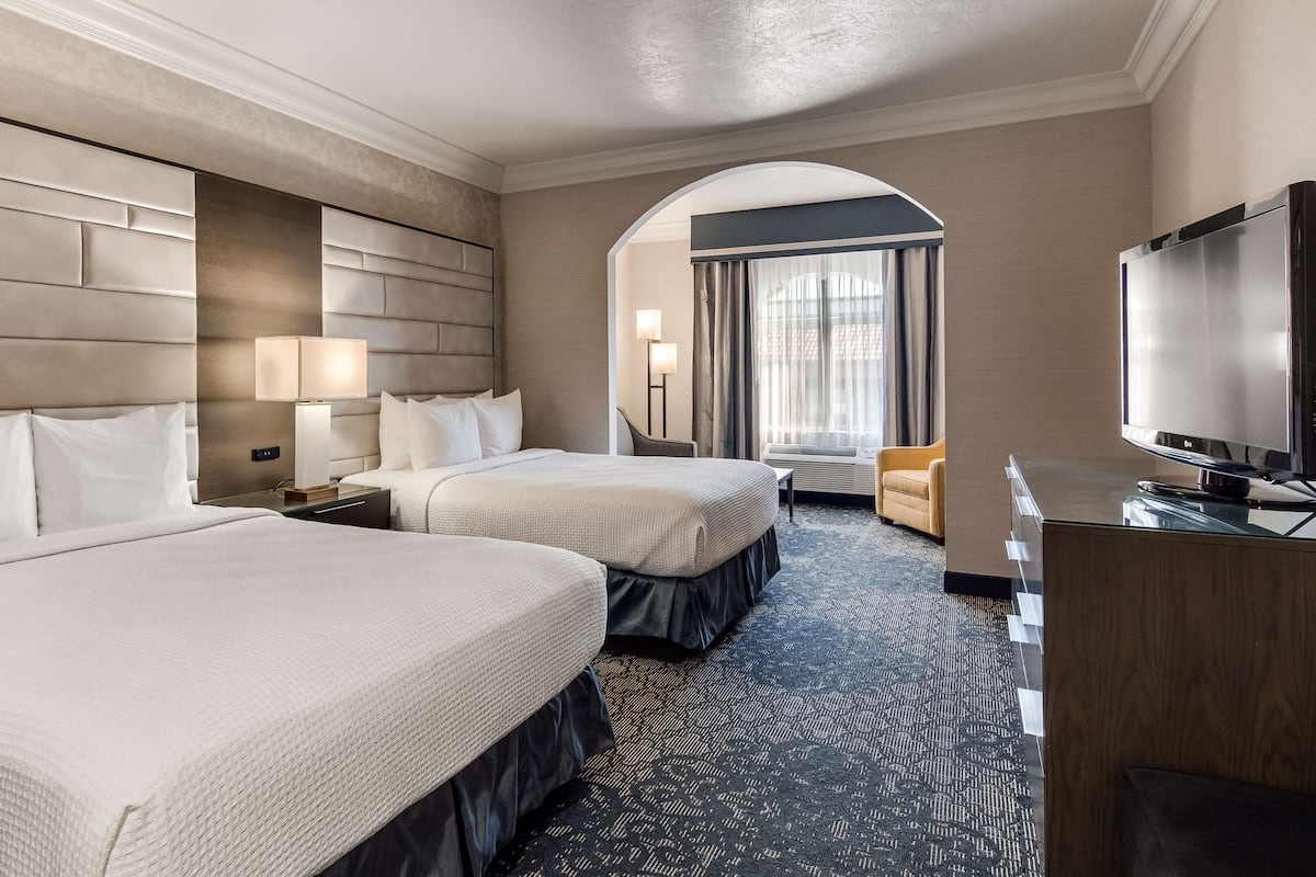 A hotel room with two beds, a desk, a television, and a view of the outside through a window.