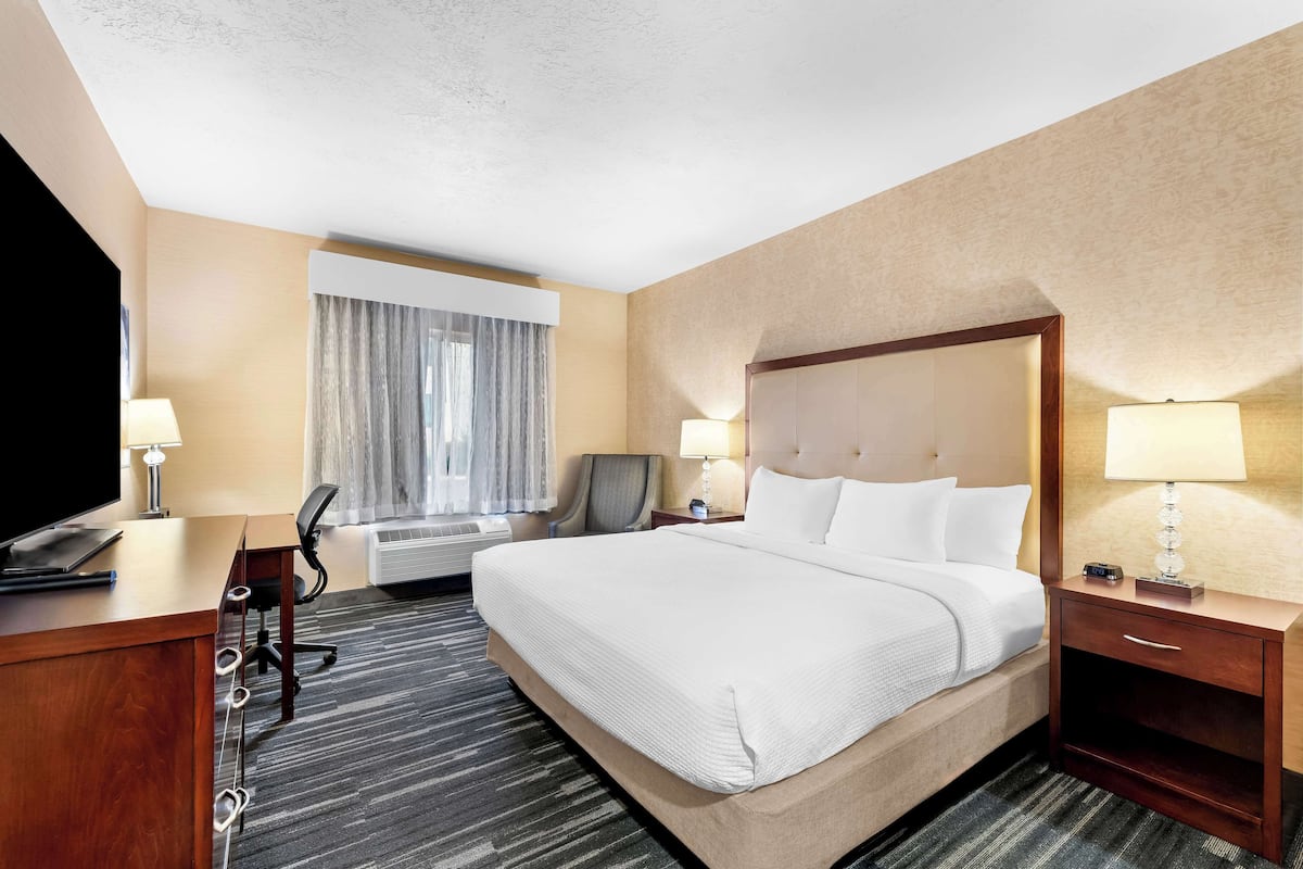 A hotel room with a large bed, a desk with a computer, a chair, a TV, and a lamp.