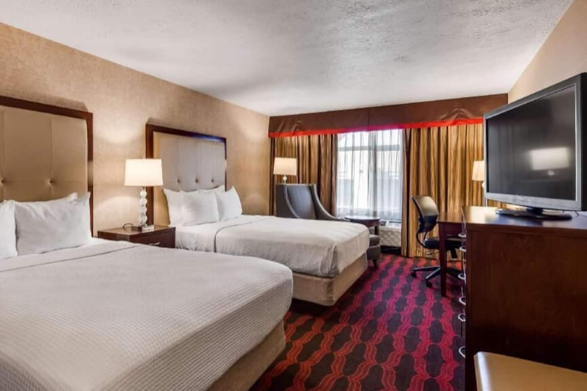 A hotel room with two beds, a television, a desk, and a chair.