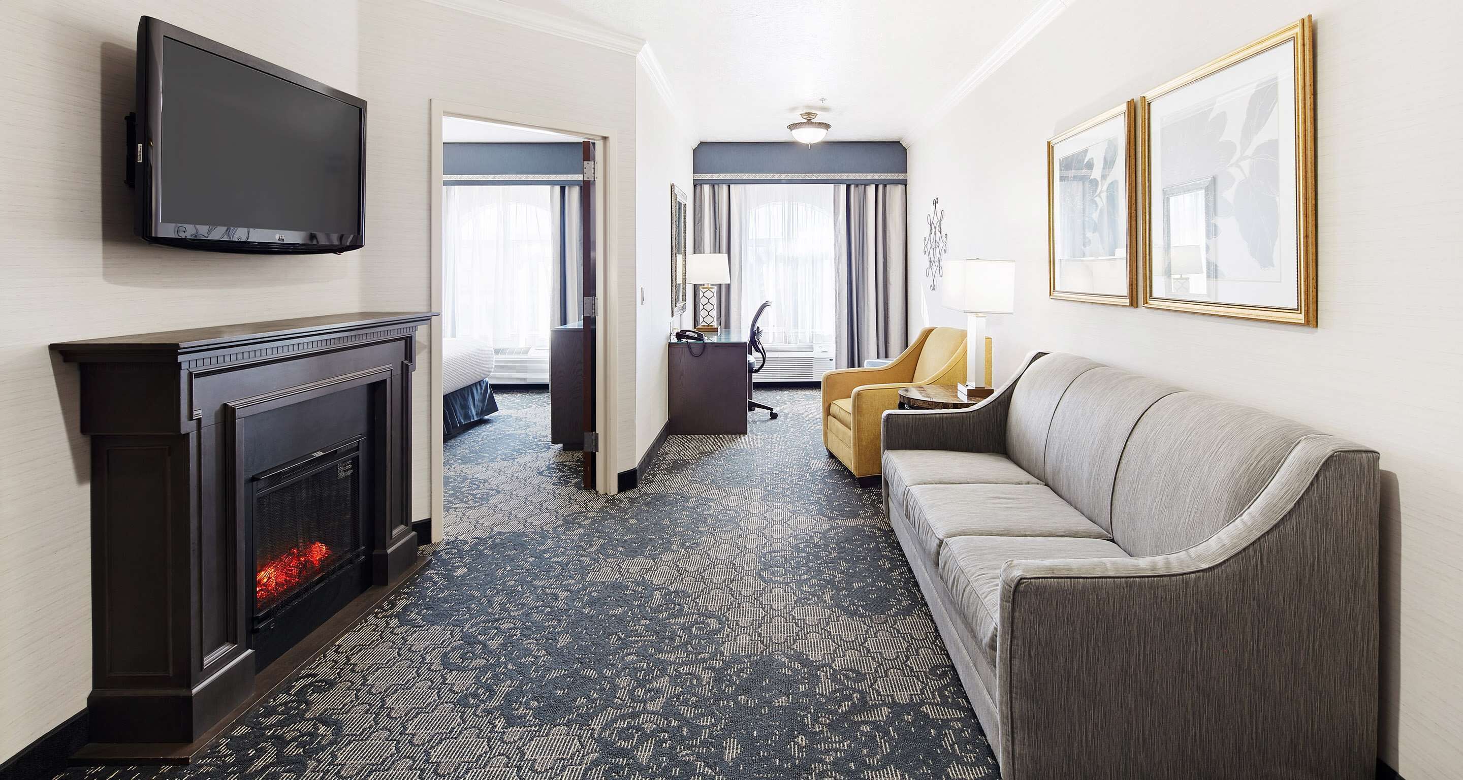 A hotel room with a fireplace, a sofa, a television, and a large window with curtains.