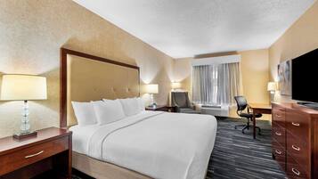 Une chambre d’hôtel avec un grand lit, un bureau, une chaise, une commode et un téléviseur.