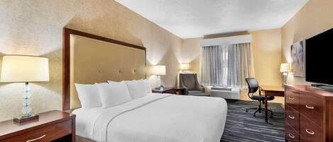 A hotel room with a large bed, a desk, a chair, a dresser, and a television.
