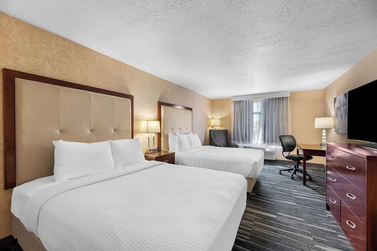 A hotel room with two beds, a desk, a chair, a TV, and a dresser.