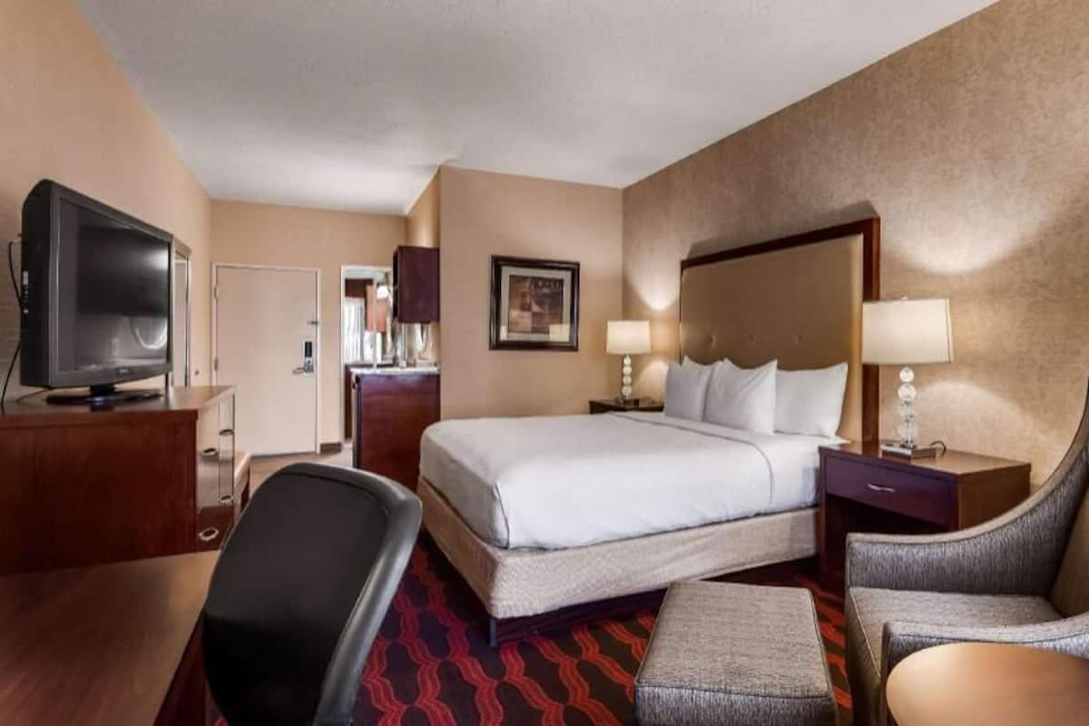 A hotel room with a bed, a TV, a desk, a chair, and a lamp.