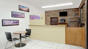 A reception area with a counter, two chairs, a table, and framed pictures on the wall. - Travelodge by Wyndham Cedar City (Cedar City)
