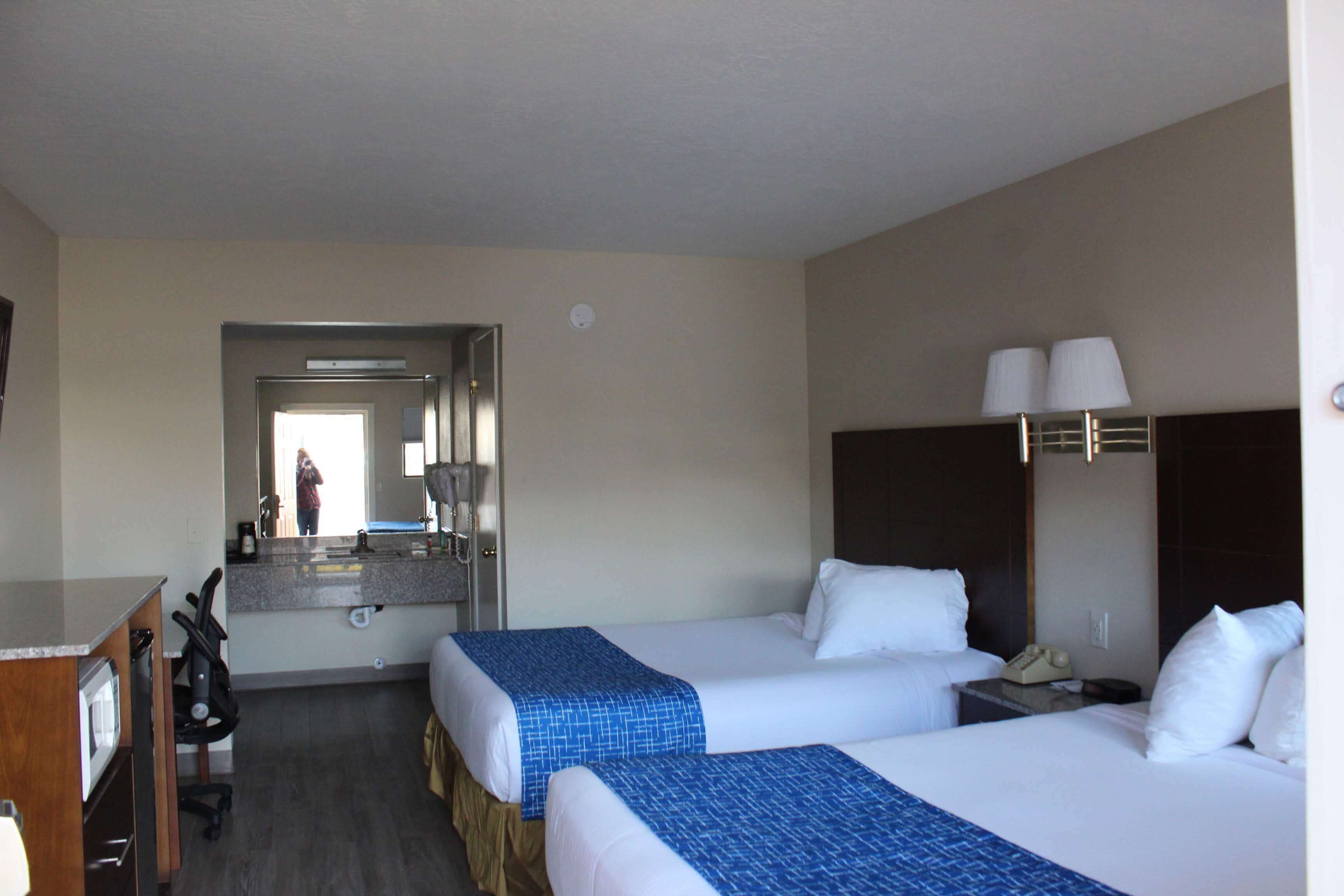 A hotel room with two beds, a desk, a chair, a mirror, and a phone on a nightstand.