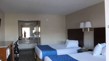 A hotel room with two beds, a desk, a chair, a mirror, and a phone on a nightstand.