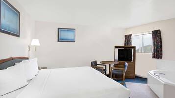 Ein Hotelzimmer mit einem großen Bett, einem Schreibtisch mit Stuhl, einem Fernseher, einem Fenster mit Vorhängen und einer Badewanne.