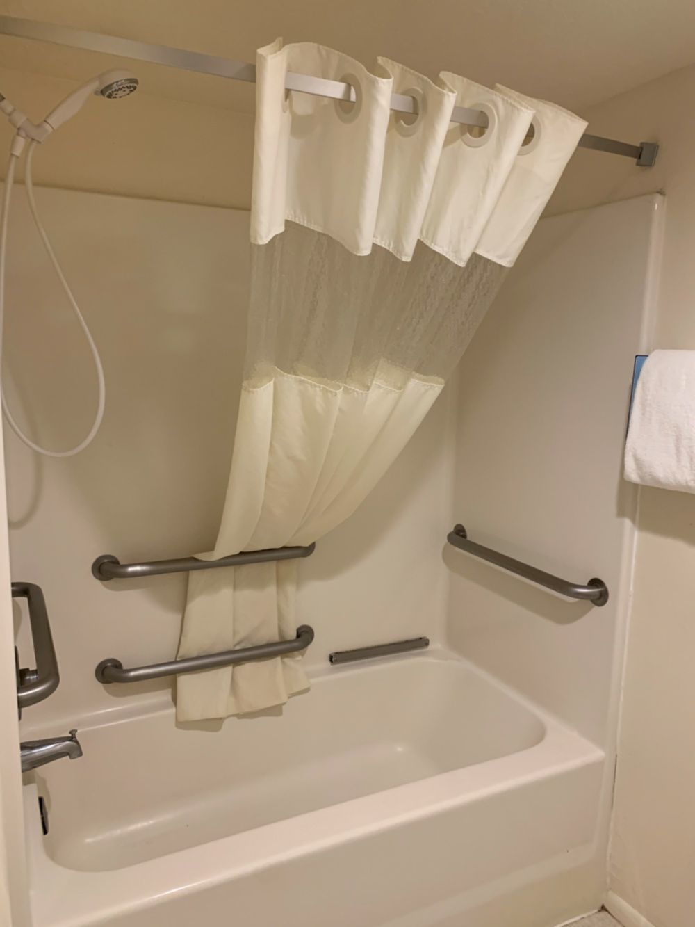 A bathtub with a showerhead, a curtain, and grab bars.