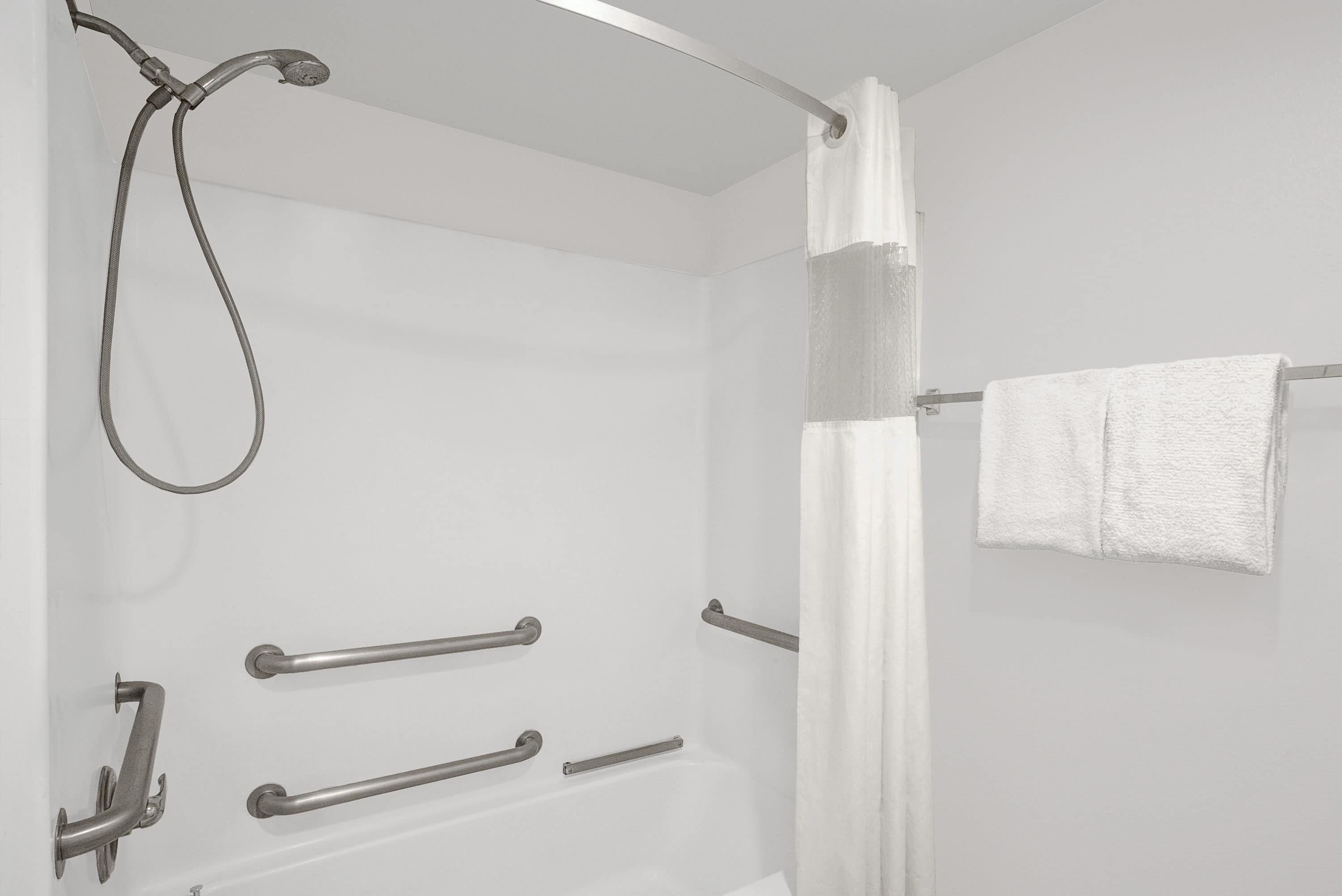 Un baño moderno con ducha, barras de apoyo y un perchero para toallas.
