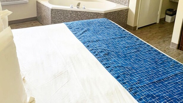 A hotel room with a large bed, a bathtub, a window with blinds, and a framed picture on the wall. - Travelodge by Wyndham Cedar City (Cedar City)