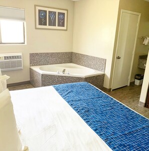 Habitación de hotel con una cama grande, una bañera, una ventana con persianas y un cuadro enmarcado en la pared.