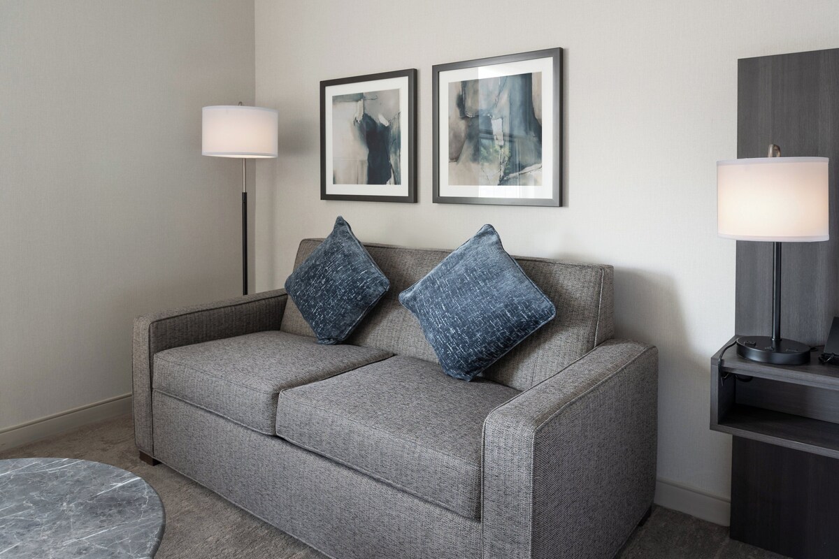A grey sofa with two blue pillows, a round marble table, and two framed abstract paintings on the wall.