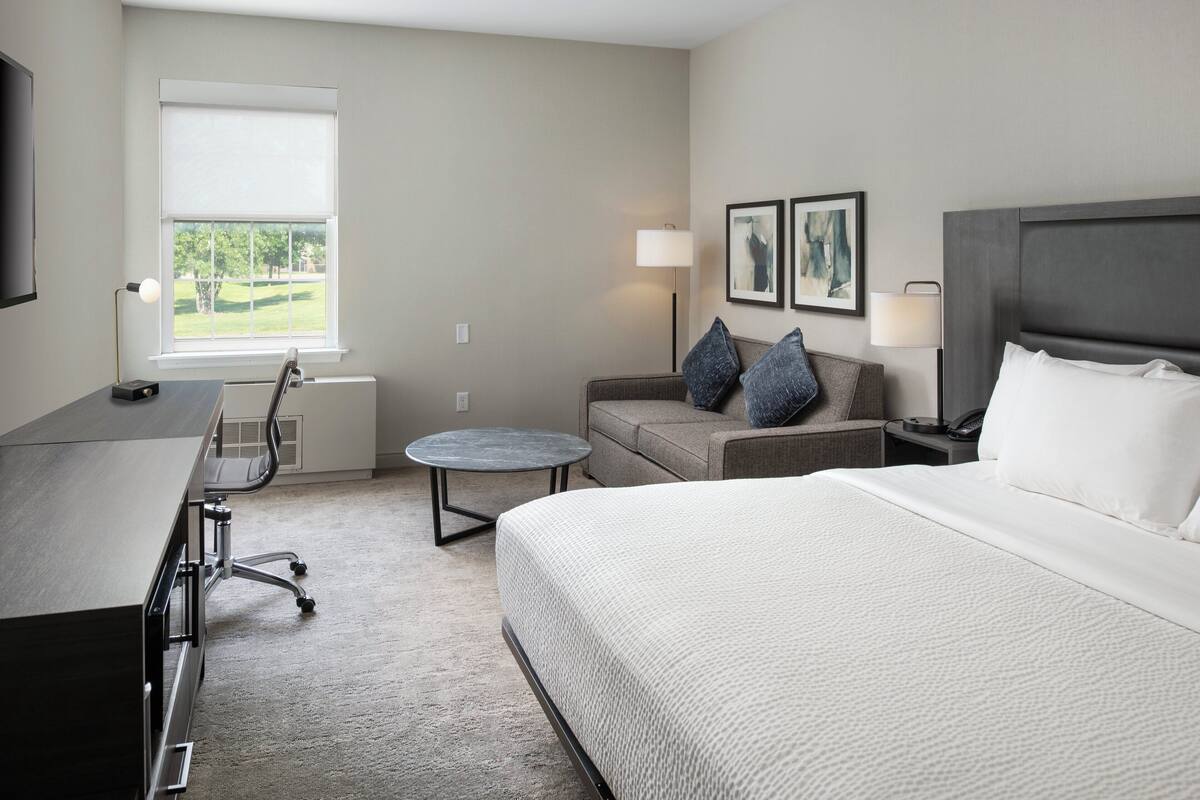 A hotel room with a bed, a desk, a chair, a small table, and a sofa.