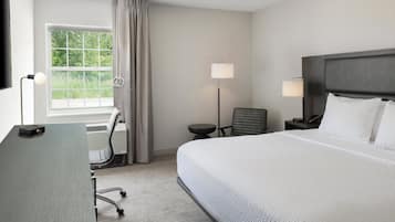 A hotel room with a large bed, a desk, a chair, a lamp, and a view of greenery through the window.