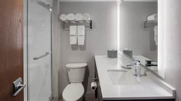 Une salle de bain moderne avec une douche à parois de verre, des toilettes blanches, un lavabo avec un miroir et des distributeurs de serviettes.
