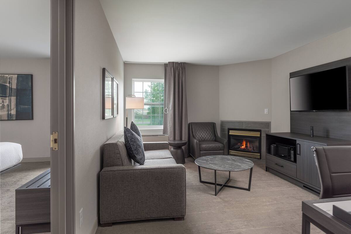 A modern living room with a sofa, armchair, coffee table, fireplace, and flat-screen TV.