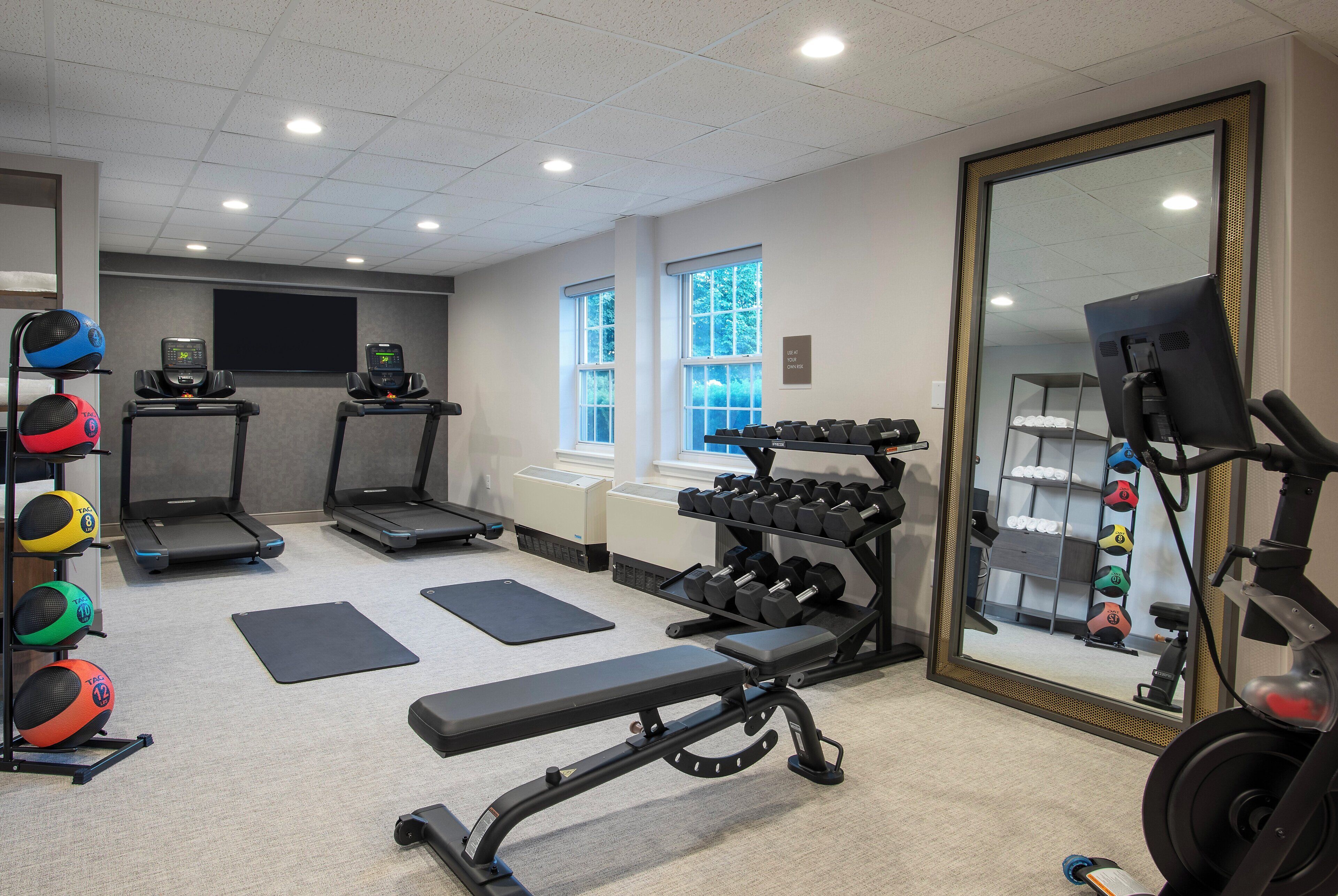 A gym with treadmills, a bench, dumbbells, and exercise balls.