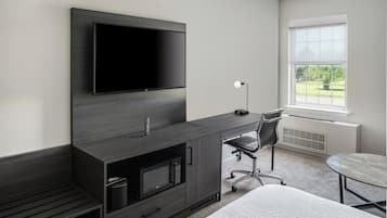 Ett modernt sovrum med en platt-TV, ett skrivbord med en stol, ett litet bord och ett fönster med utsikt över grönområden.