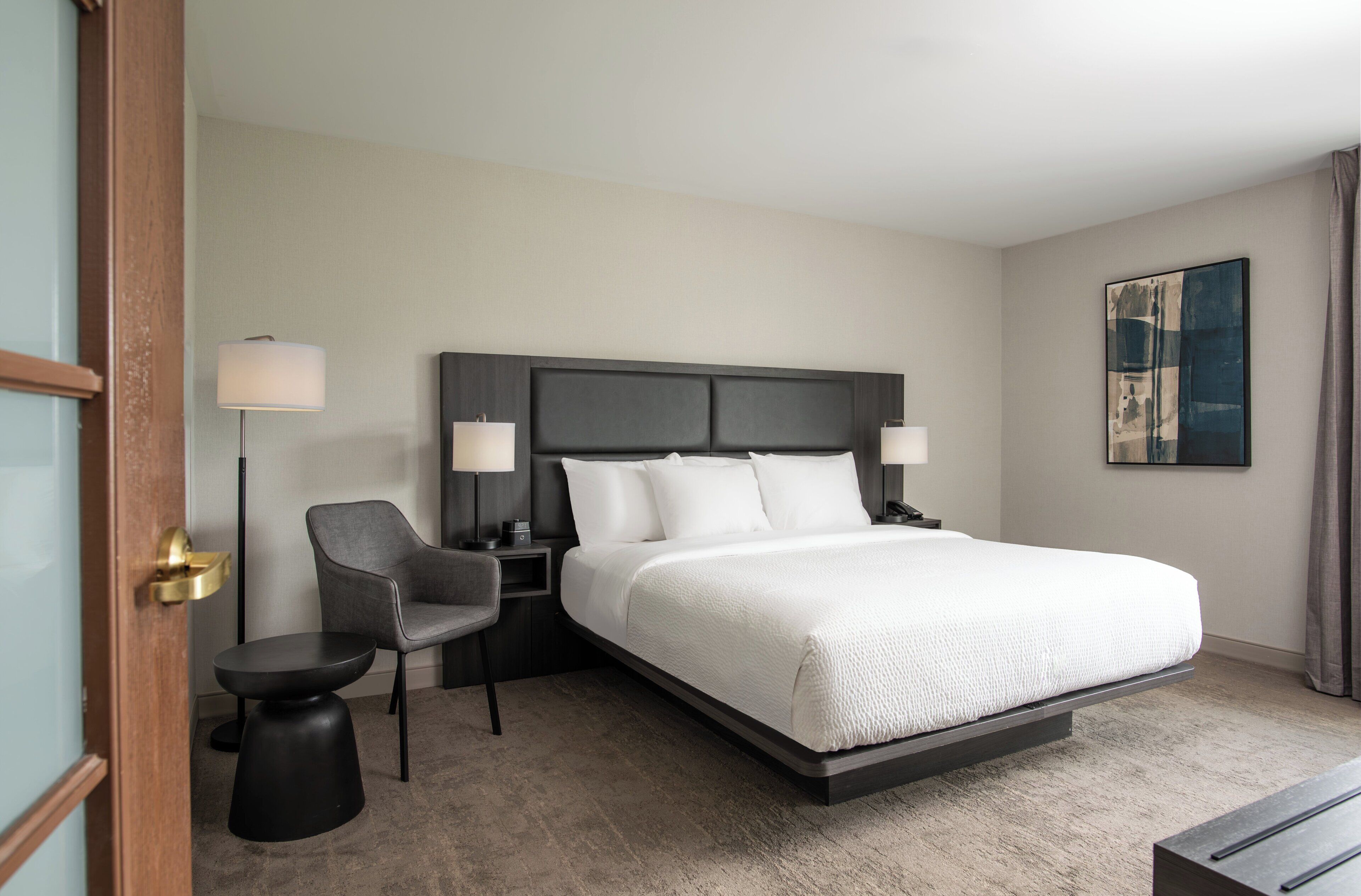 Ein modernes Hotelzimmer mit einem großen Bett, einem Schreibtisch, einem Stuhl und einer Lampe.