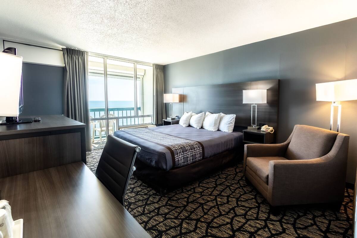 Quarto de hotel com uma cama grande, uma escrivaninha, uma cadeira e vista para o oceano.