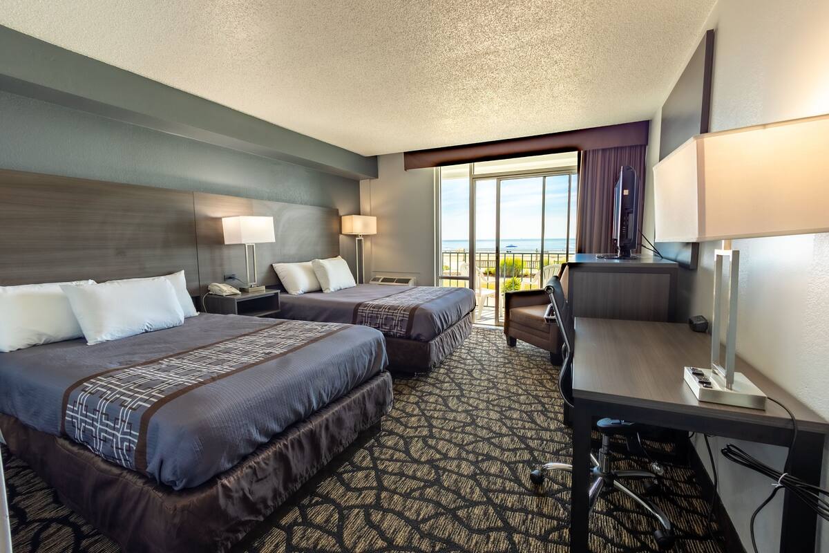Quarto de hotel com duas camas, uma escrivaninha, um computador e vista para o oceano.