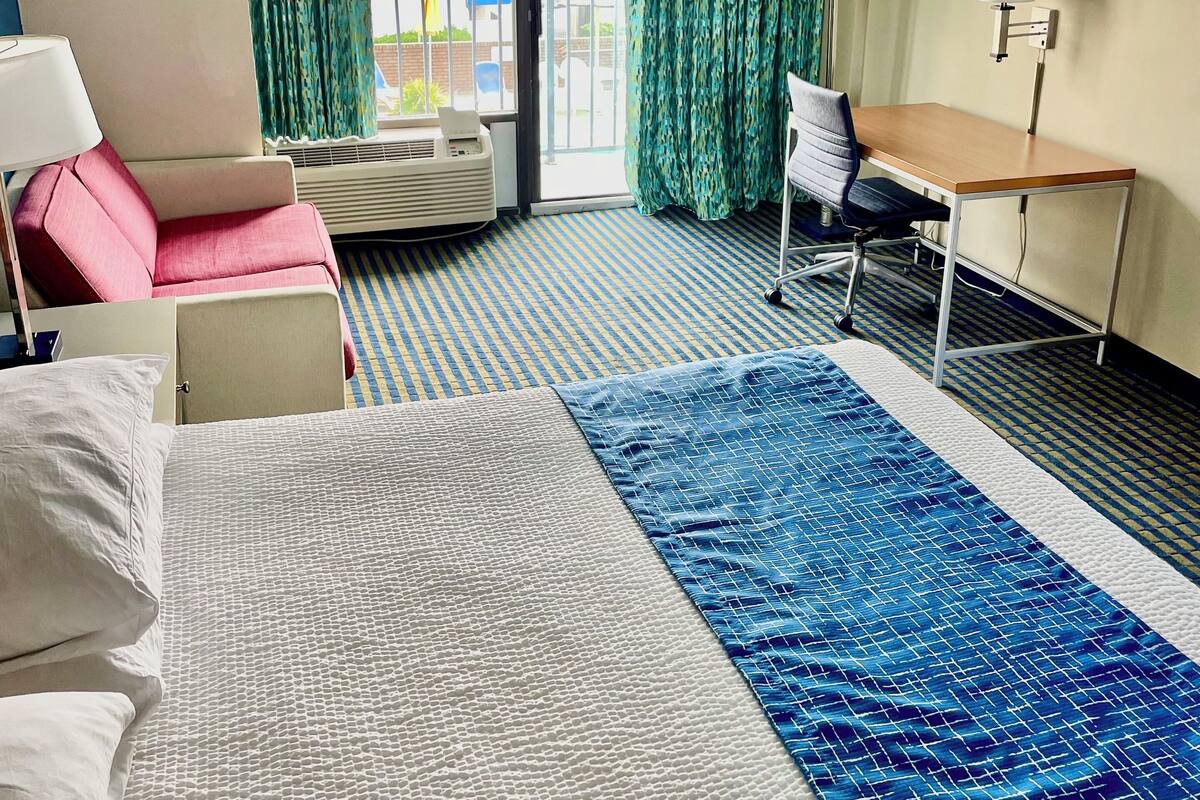 A hotel room with a bed, a desk, a chair, a window with curtains, and a view of the outside.