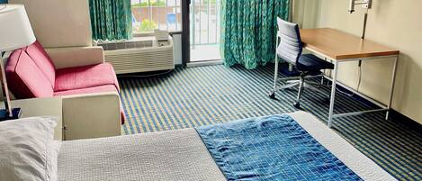 A hotel room with a bed, a desk, a chair, a window with curtains, and a view of the outside.