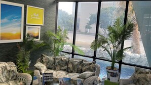 A modern lounge area with wicker furniture, large windows, and tropical plants. - Days Inn by Wyndham Virginia Beach At The Beach (Virginia Beach)