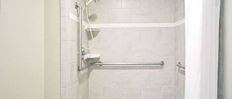 A shower with a grab bar, tiled walls, and a showerhead.