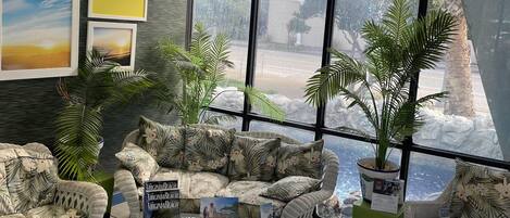 Una habitación con mobiliario de mimbre, una mesa de centro de vidrio y ventanas amplias con vistas al exterior.