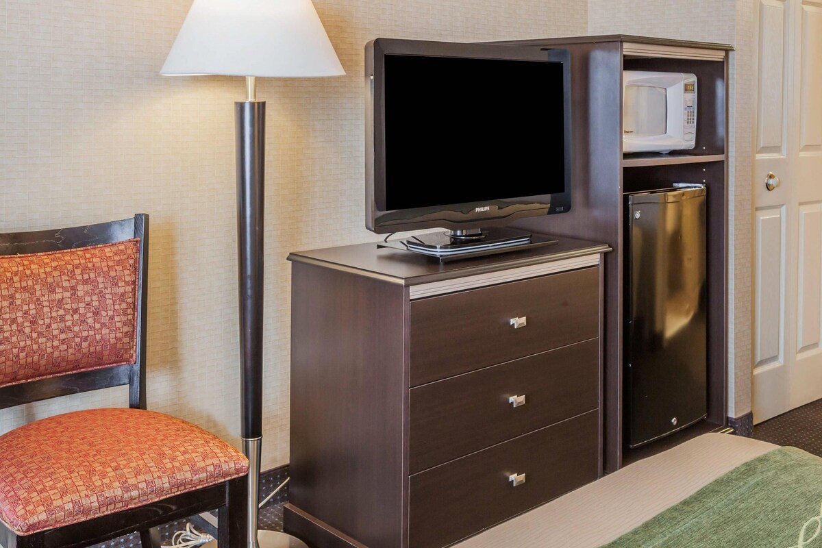 Ein Hotelzimmer mit Flachbildfernseher, einer Mikrowelle, einer Minibar, einem Schreibtisch und einem Sessel.