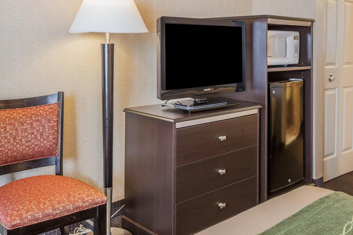 A hotel room with a television, microwave, minibar, and a chair.