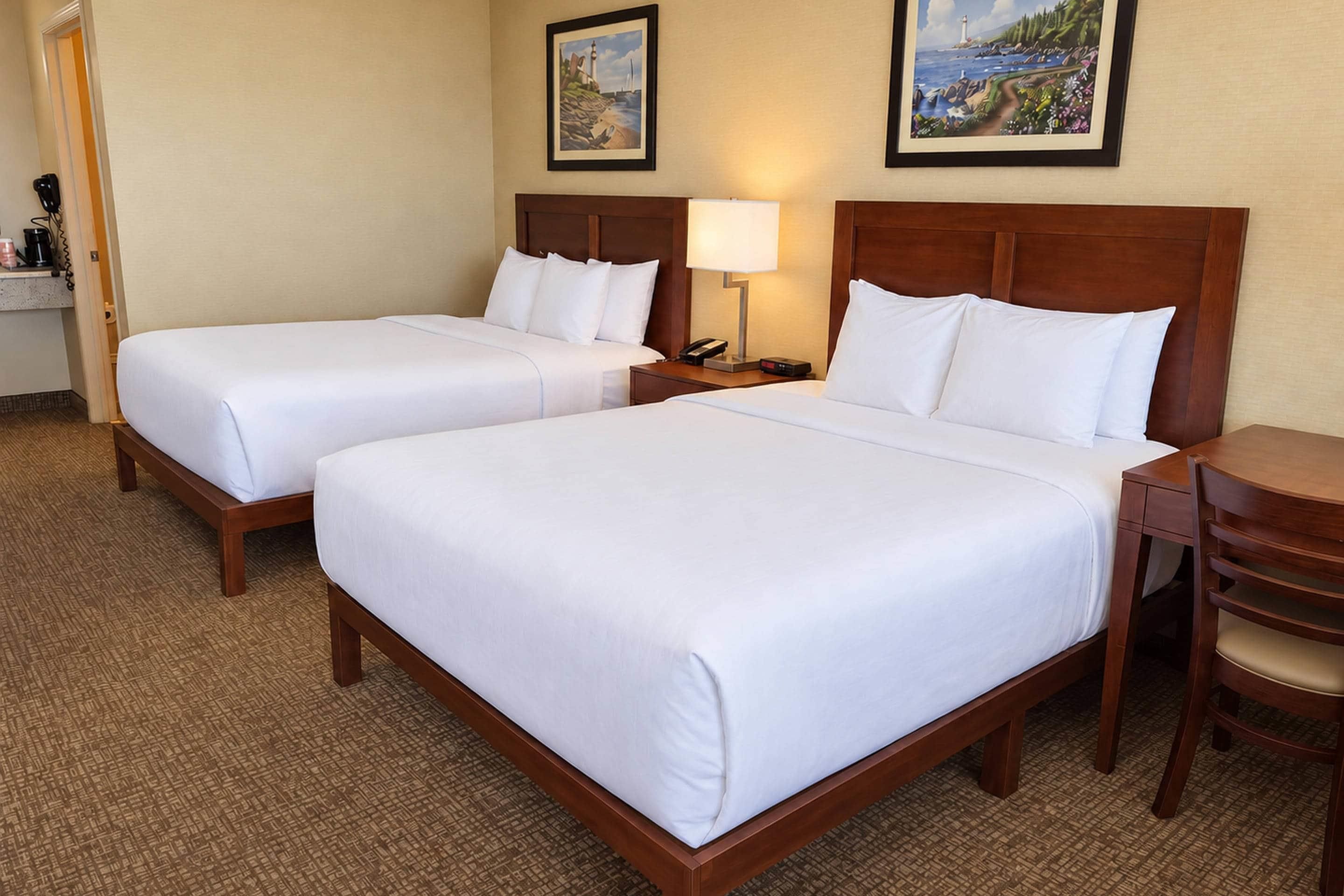 A hotel room with two single beds, a bedside table with a lamp, a chair, and a small desk with a telephone.