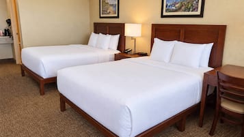 A hotel room with two single beds, a bedside table with a lamp, a chair, and a small desk with a telephone.