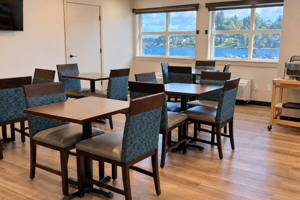 A conference room with multiple tables and chairs, large windows with a view of the sea, and a door. - Comfort Inn On the Bay (Port Orchard)