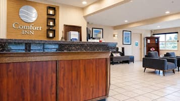 A reception area with a wooden reception desk, a sign reading 'Comfort Inn,' and a seating area with chairs and a sofa.