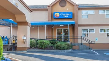 De ingang van een Comfort Inn hotel, met een blauw luifel, een brievenbus en een parkeerplaats.