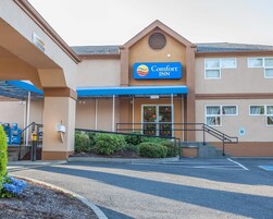 Entrada de un hotel Comfort Inn con un toldo azul, un buzón y un estacionamiento.